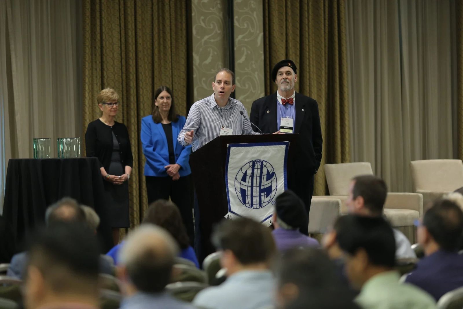 A presenter speaking at an AIS-bannered podium during an awards ceremony