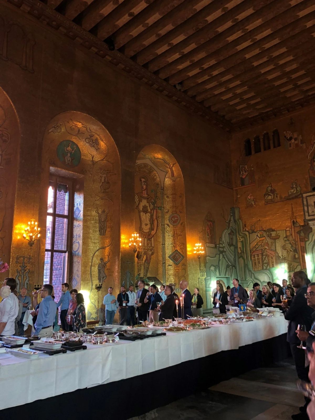 Conference attendees gathered at a reception in a gilded mosaic hall