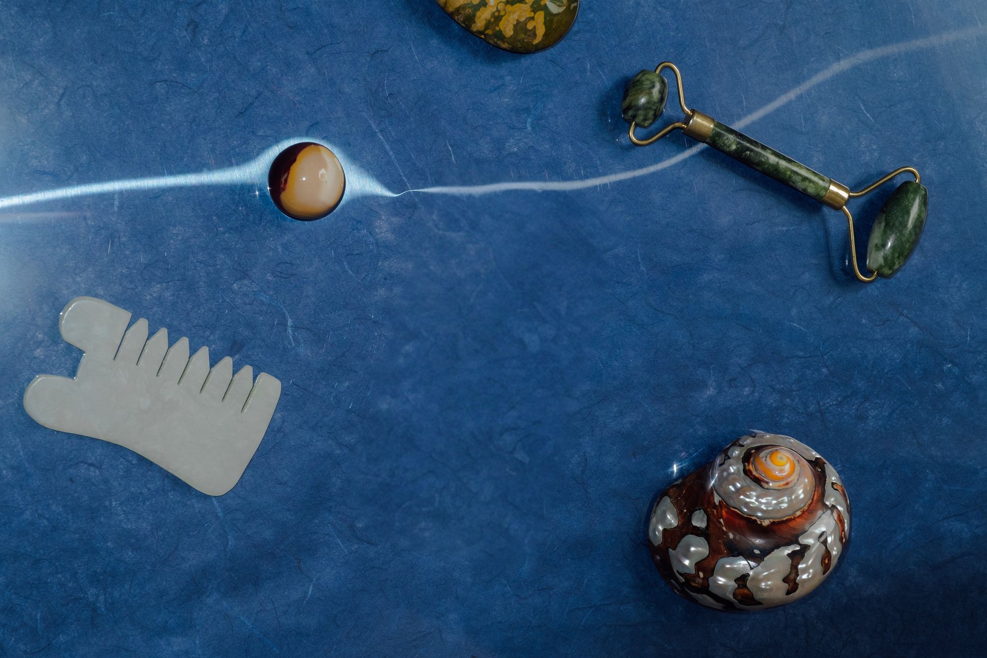 Stones, a shell and a jade roller resting on deep blue handmade paper